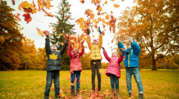 Children throwing orange autumnal leaves into the air and jumping